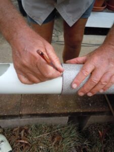 Marking and cutting the pipe by hand using a piece of lino as a guide.